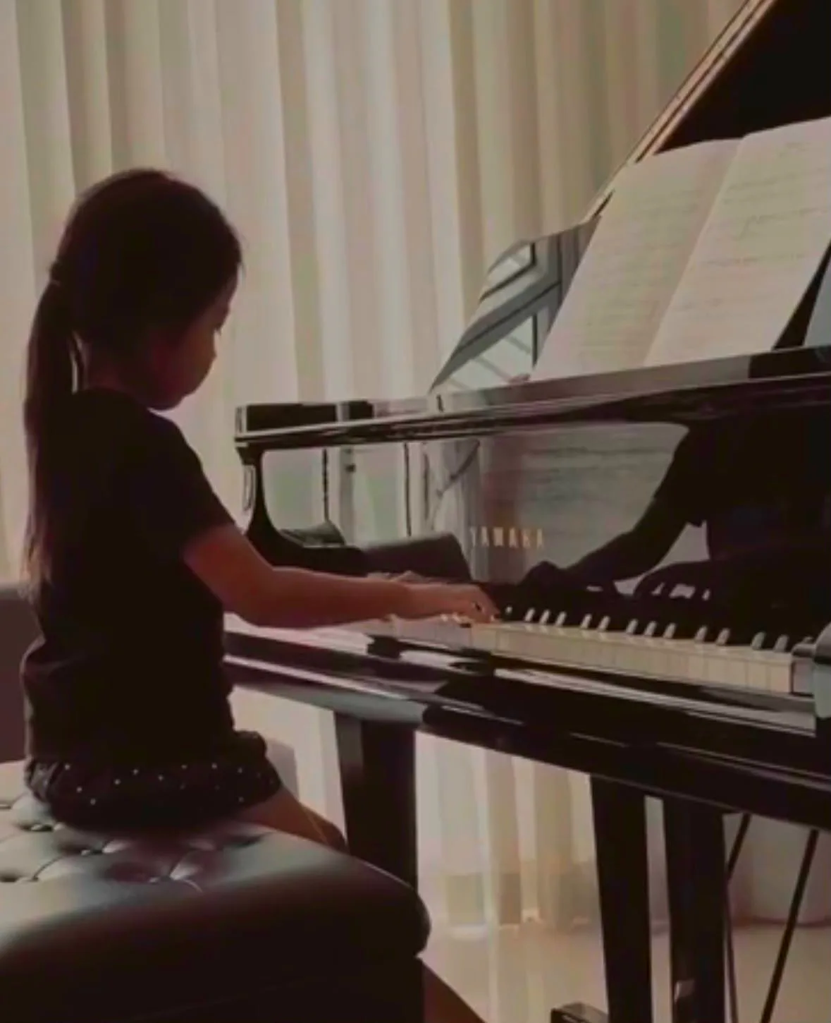 A young girl practising at a Yamaha grand piano at home