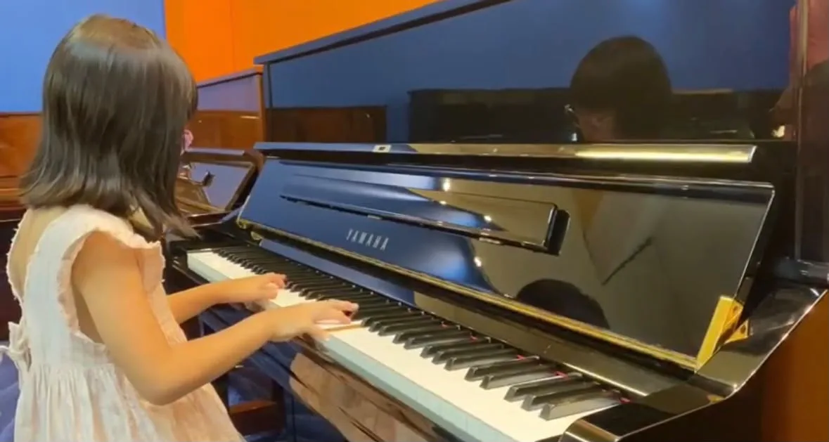A young girl playing a Yamaha upright piano in the viewing gallery